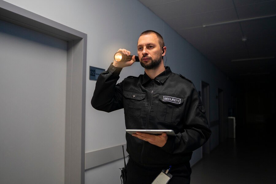 A security guard using his flashlight to navigate through a dark corridor.