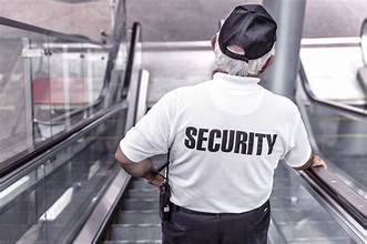A security guard facing away from the camera and riding the escalator down.