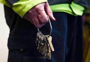 A security guard with a green jacket holding a bunch of keys in their hand.
