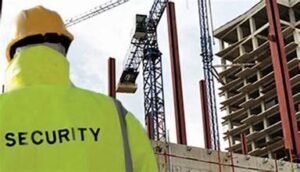 A security guard looking at a crane and a building with his back towards the camera.