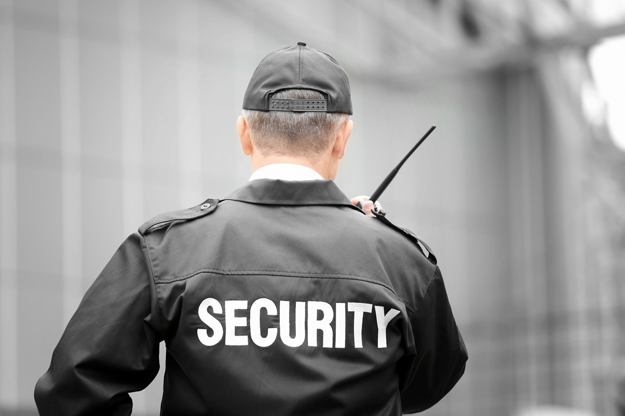 A security guard showing his back towards the camera and talking on his radio.