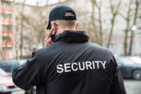 A security guard facing away from the camera as he answers to a call on his radio.