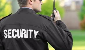 A security guard looking away from the camera towards his right and talking on the radio.